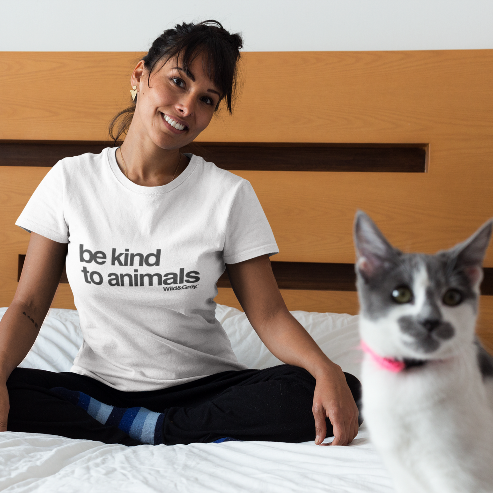 Woman wearing a 'be kind to animals' shirt sitting on a bed with a cat.