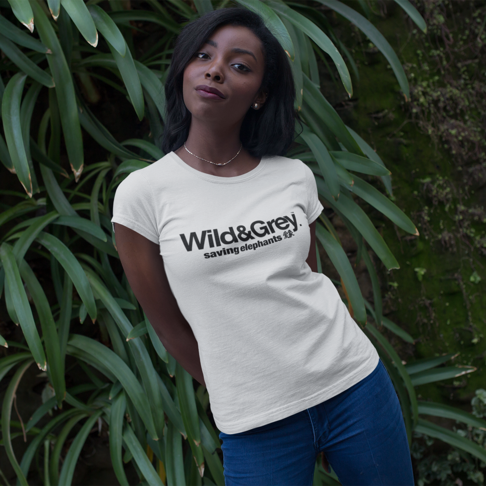 Woman wearing a 'Wild&Grey' t-shirt standing in front of green foliage